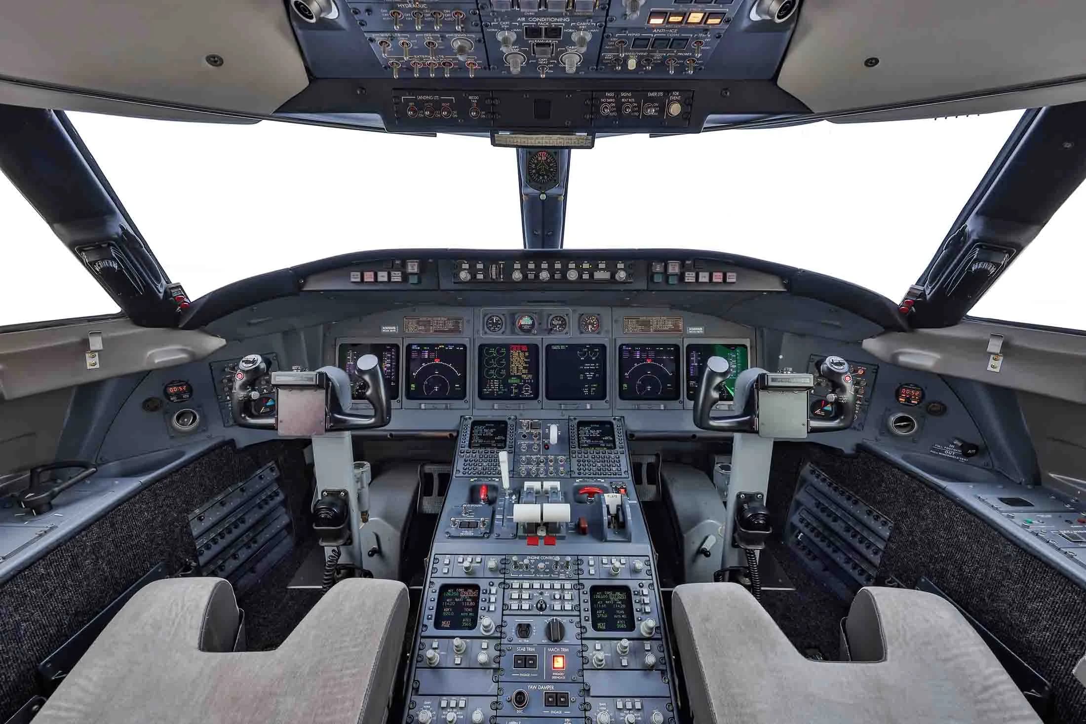 The spacious cockpit of a business jet, featuring multiple digital displays, control yokes, and a central throttle quadrant.