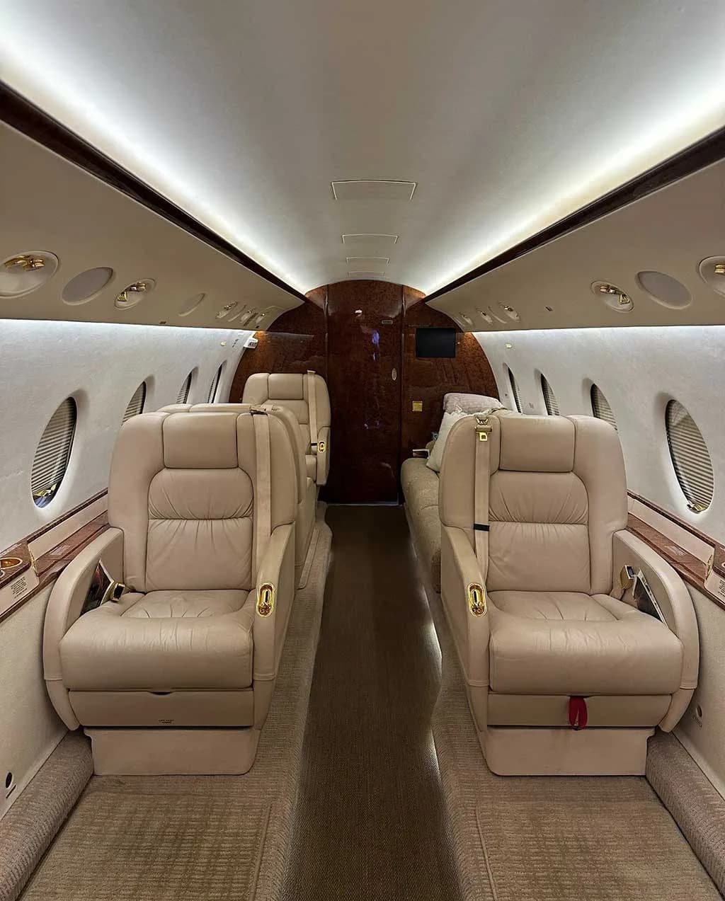 The luxurious interior cabin of a business jet, featuring beige leather seats and wood paneling.