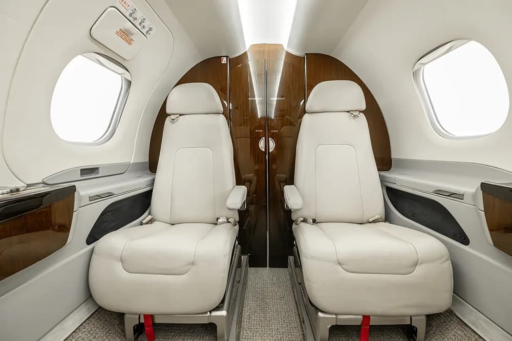 A view of the rear white leather seats in a private jet cabin, facing a dark wood partition.