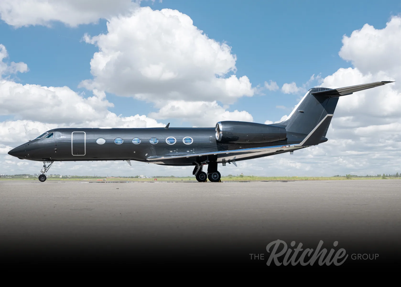 A dark grey Gulfstream G650 business jet parked on a tarmac under a partly cloudy sky, viewed from the side.