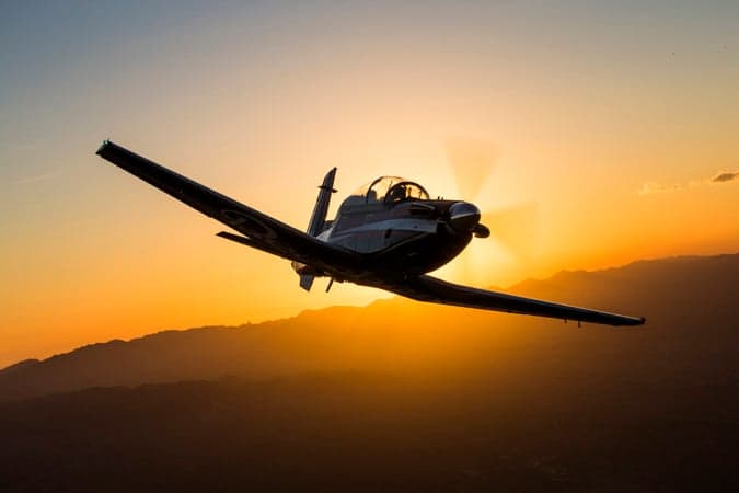A Beechcraft T-6C Texan II aircraft silhouetted against a bright sunset.