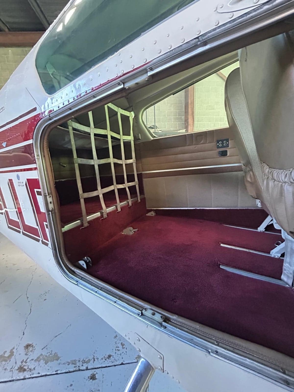 The open rear door of an aircraft revealing a red carpeted cargo area with a white net.