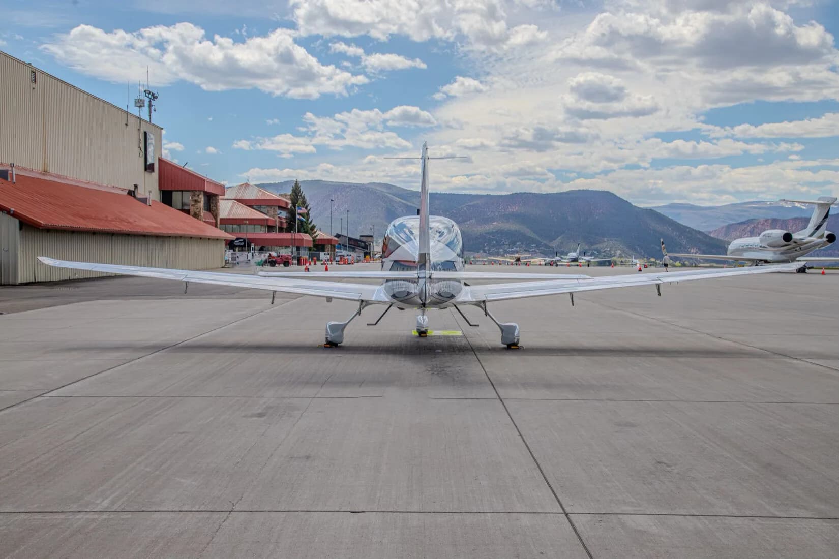 Rear view of a blue and white Cirrus SR22T GTS aircraft, registration N332RM, parked on an airport tarmac with other aircraft and buildings in the distance.