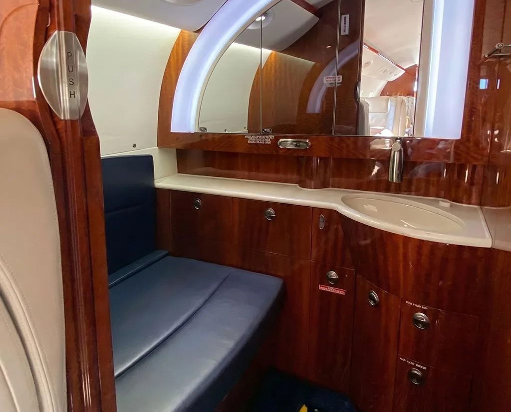 The aircraft lavatory features a sink, mirror, and rich wooden cabinetry.