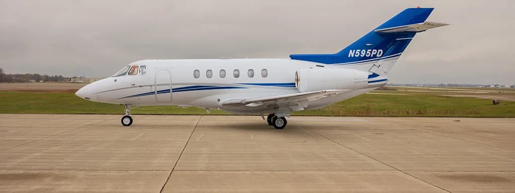 A white business jet with blue and silver stripes on the tail and fuselage, parked on a concrete tarmac under an overcast sky.