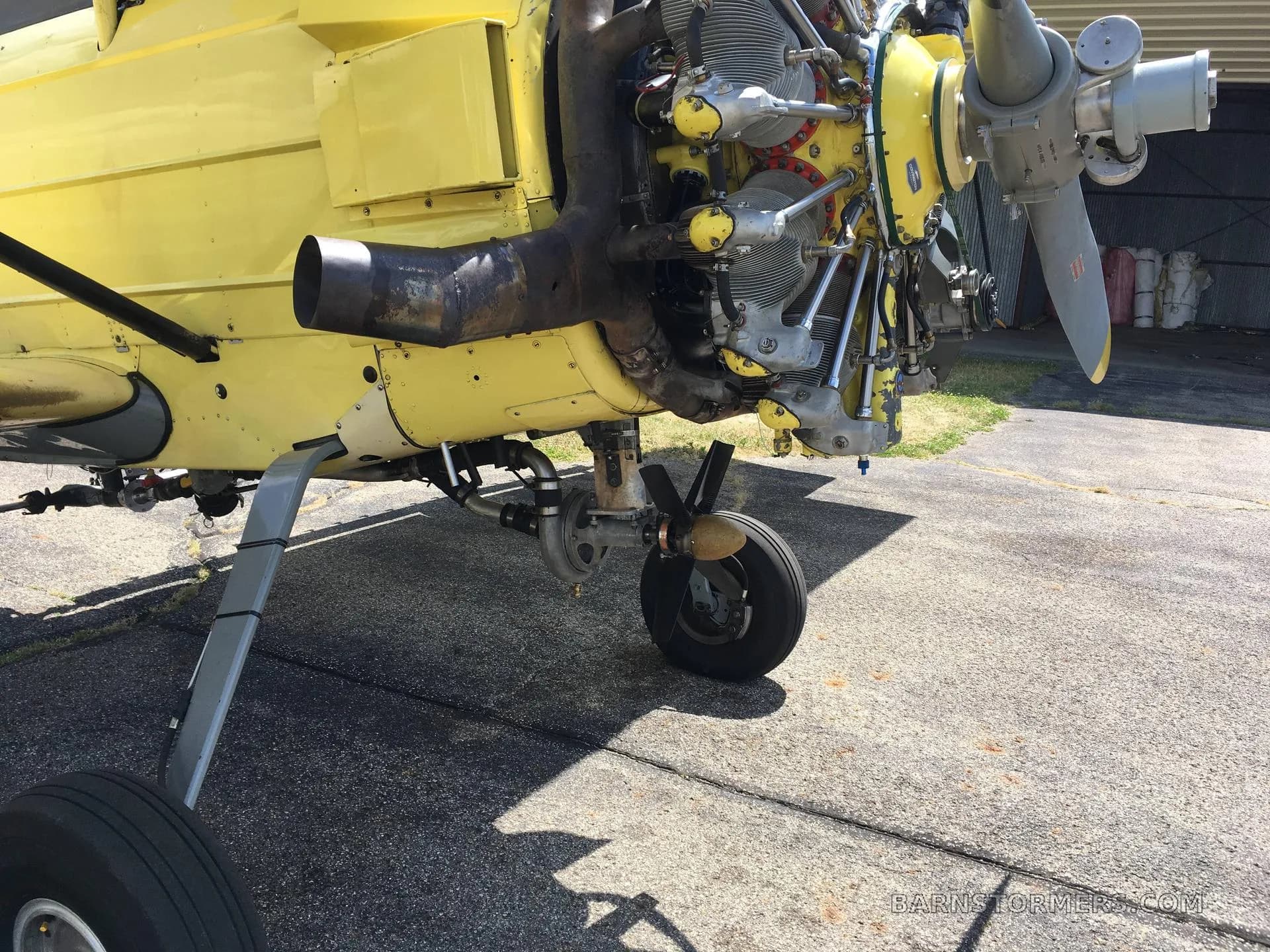 A close-up view of the exposed radial engine, propeller, and front landing gear of a yellow biplane crop duster.