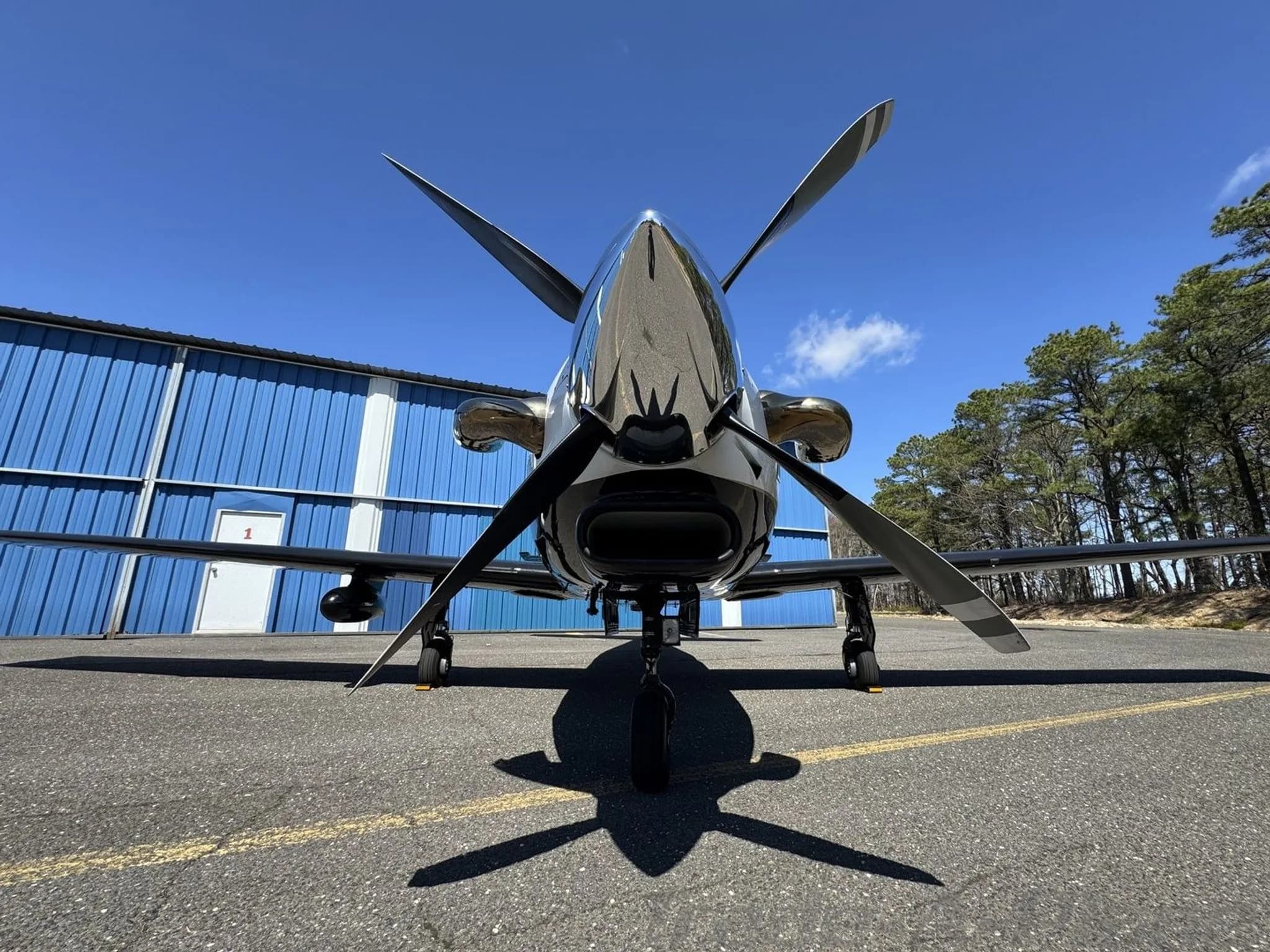 A close-up, low-angle front view of the propeller and shiny nose of a white and black Piper M-class aircraft.