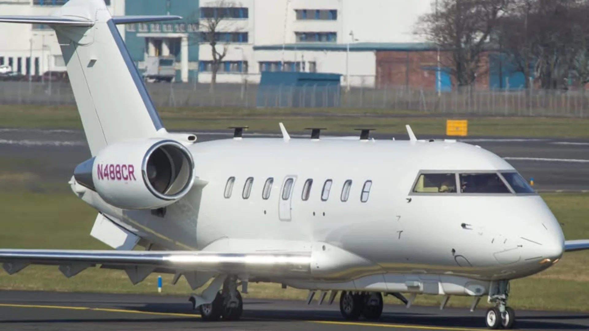 A close-up side view of a white Bombardier Challenger 605 business jet, registration N488CR, on an airport tarmac.