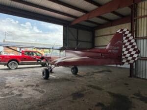 Side view of a red Cubcrafters aircraft with a checkered tail in a hangar.