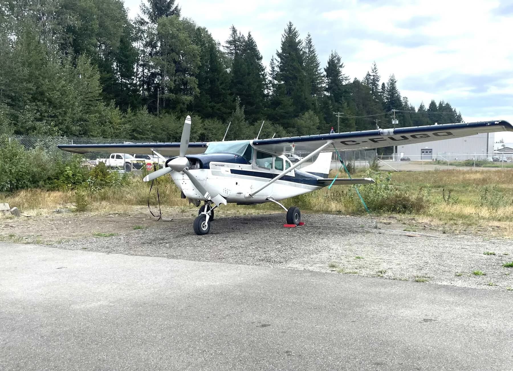 A Cessna 206 Stationair parked on a gravel area near trees.