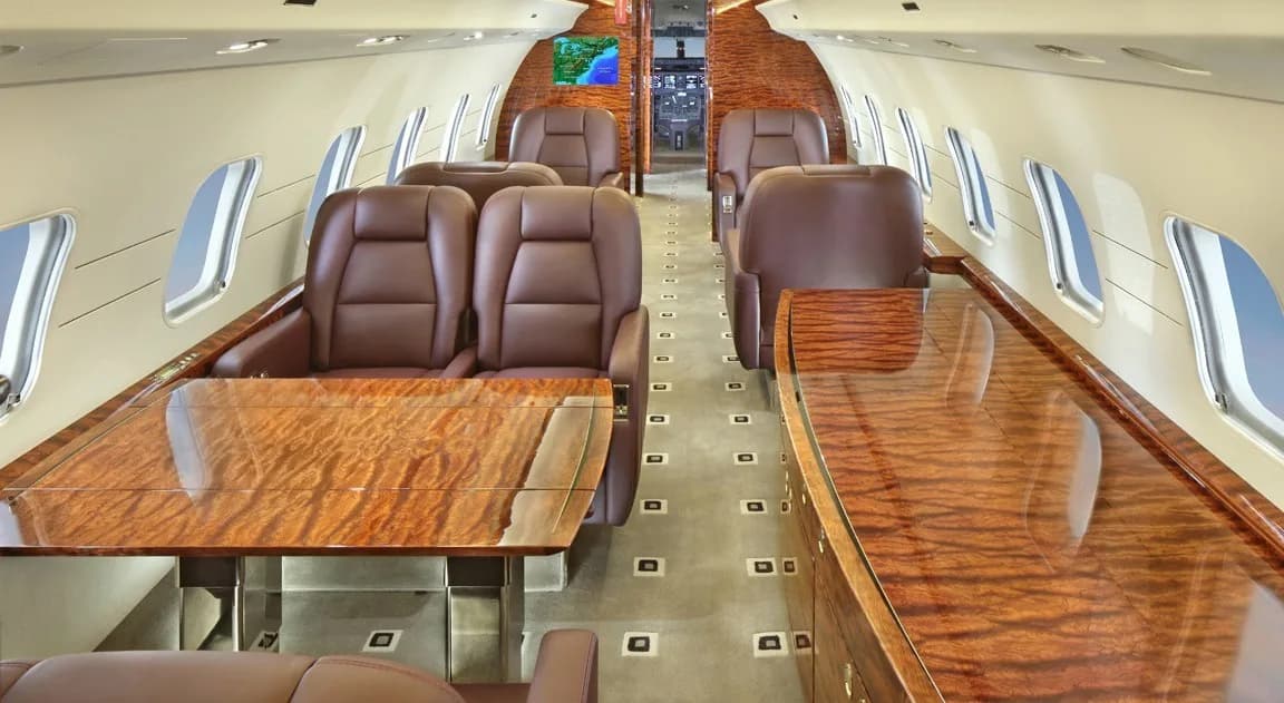 The interior of a Bombardier Challenger aircraft with leather seats and wood trim.