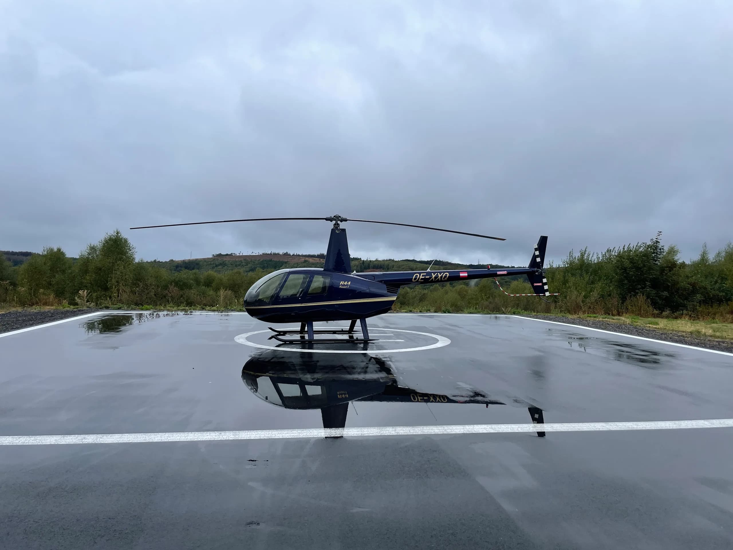 Robinson R44 Raven I OE-XXQ helicopter on a helipad on a cloudy day.