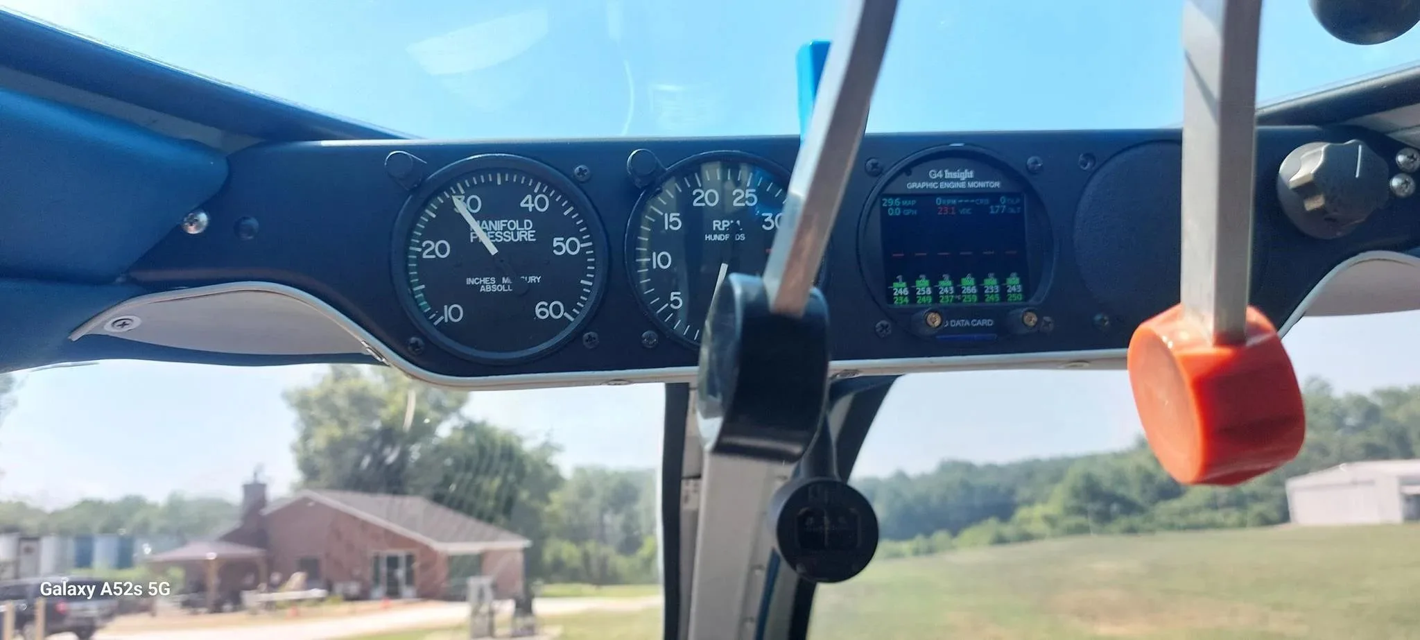 A view from the cockpit showing engine gauges and the landscape through the windshield.