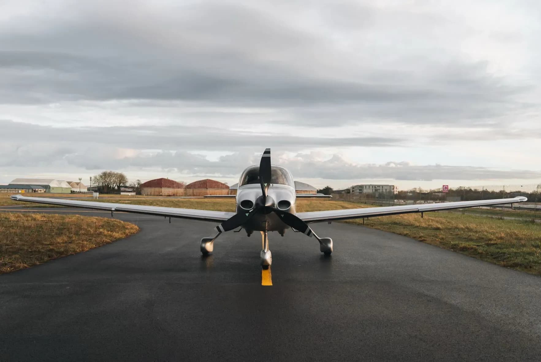 A silver and red Cirrus SR22 aircraft viewed from the front, parked on an airfield under a cloudy sky.