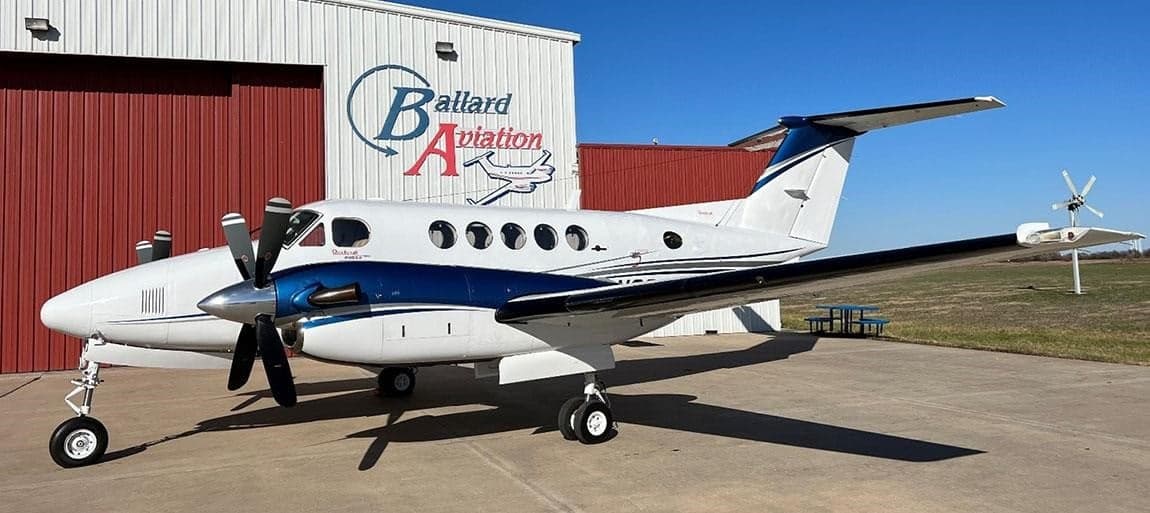 A Beechcraft King Air with a white and blue paint scheme is parked outside a hangar.