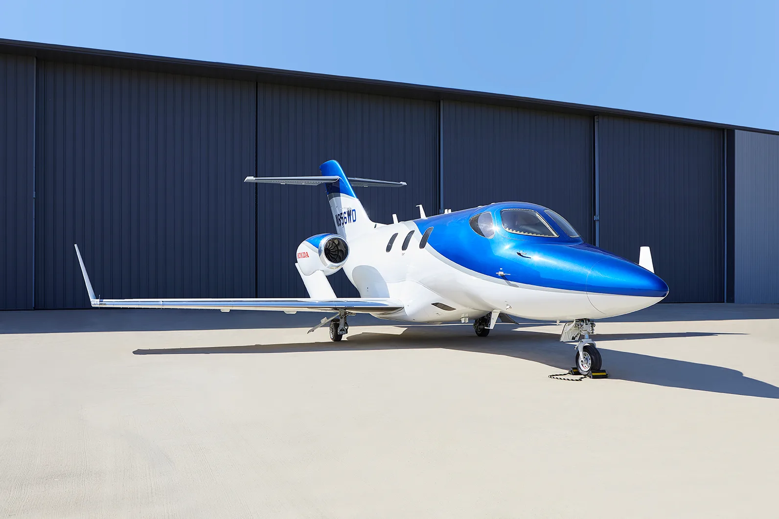 Side view of a blue and white HondaJet N856WD parked on an airfield in front of a hangar.
