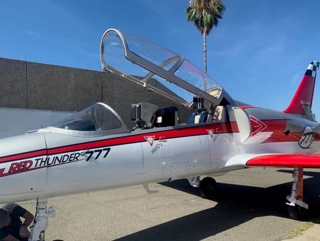 A silver and red jet with "RED THUNDER 777" markings sits on an tarmac with its canopy open.