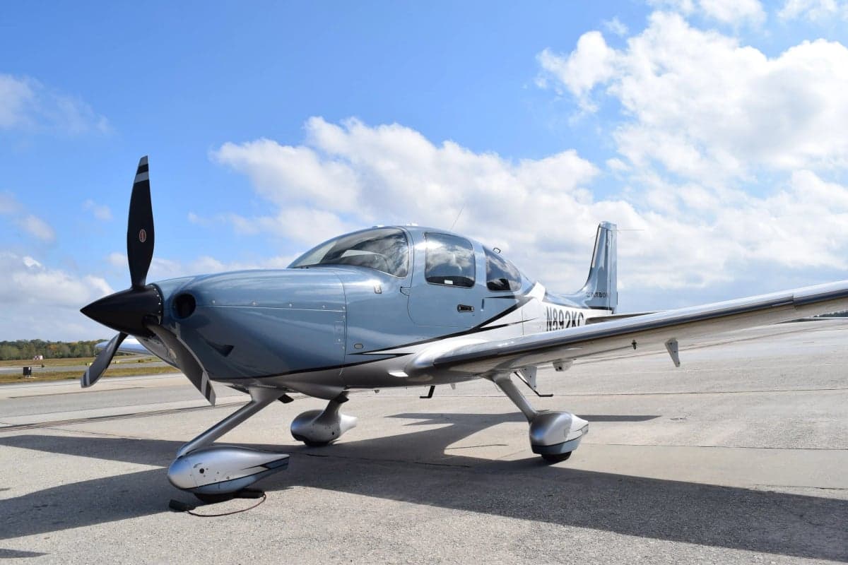 A Cirrus SR22T aircraft with a blue and silver paint scheme is parked on the tarmac.