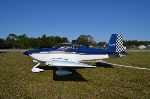 A blue and white aircraft with a checkered tail is parked on a grassy field.