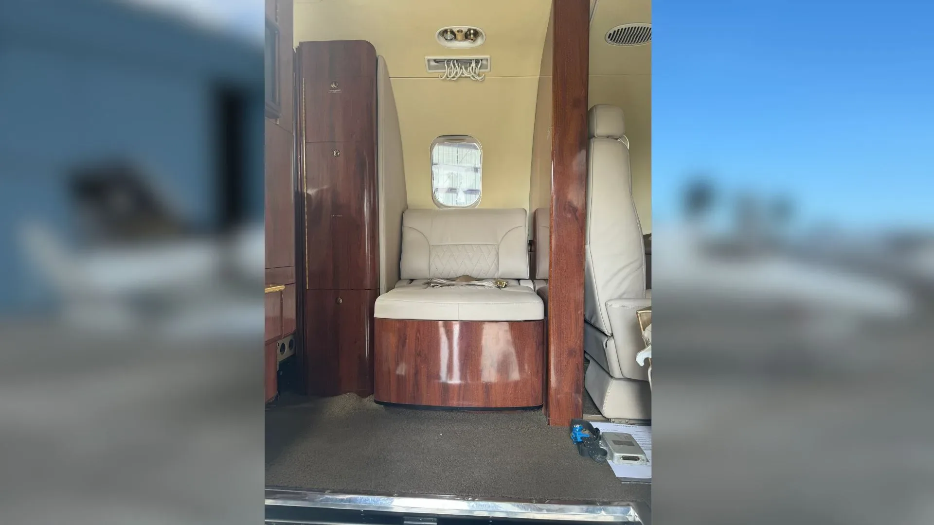 View of the Learjet 35A cabin with a wooden cabinet and light-colored leather seat.