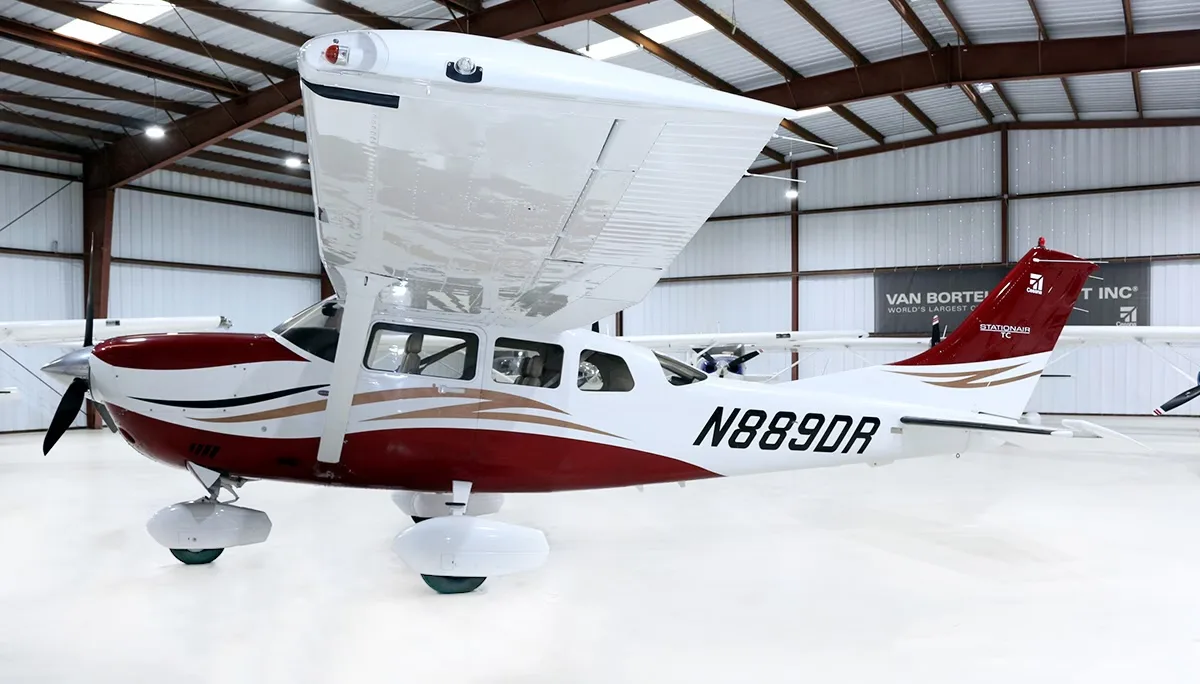 A red and white Cessna Stationair TC aircraft (N889DR) with gold accents, parked in a hangar.
