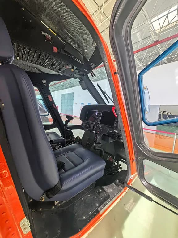 View into the helicopter cockpit showing a blue pilot's seat and part of the instrument panel.