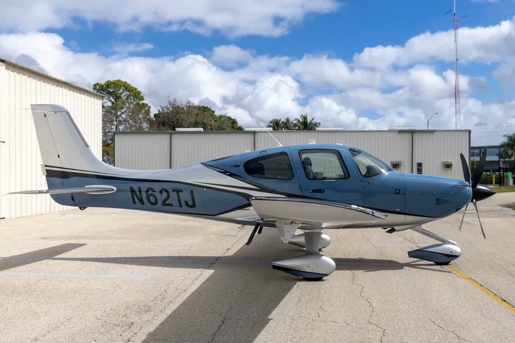 A side view of a blue and silver Cirrus SR22T aircraft with registration N62TJ parked on an airfield.