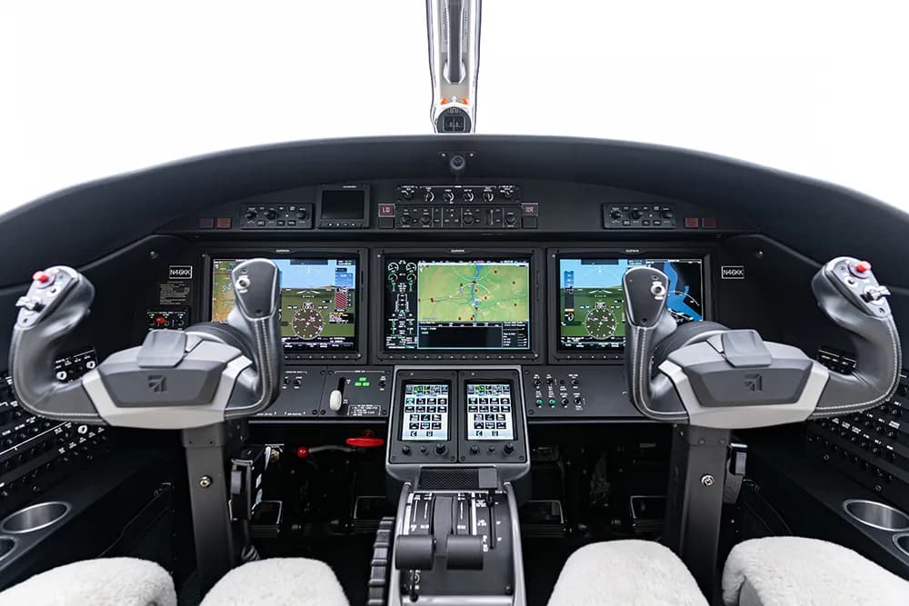 A detailed view of a modern aircraft cockpit with multiple display screens and control yokes.