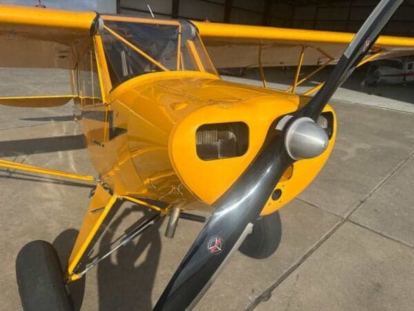 Front view of a yellow Legend Cub aircraft with a black propeller, parked in a hangar.