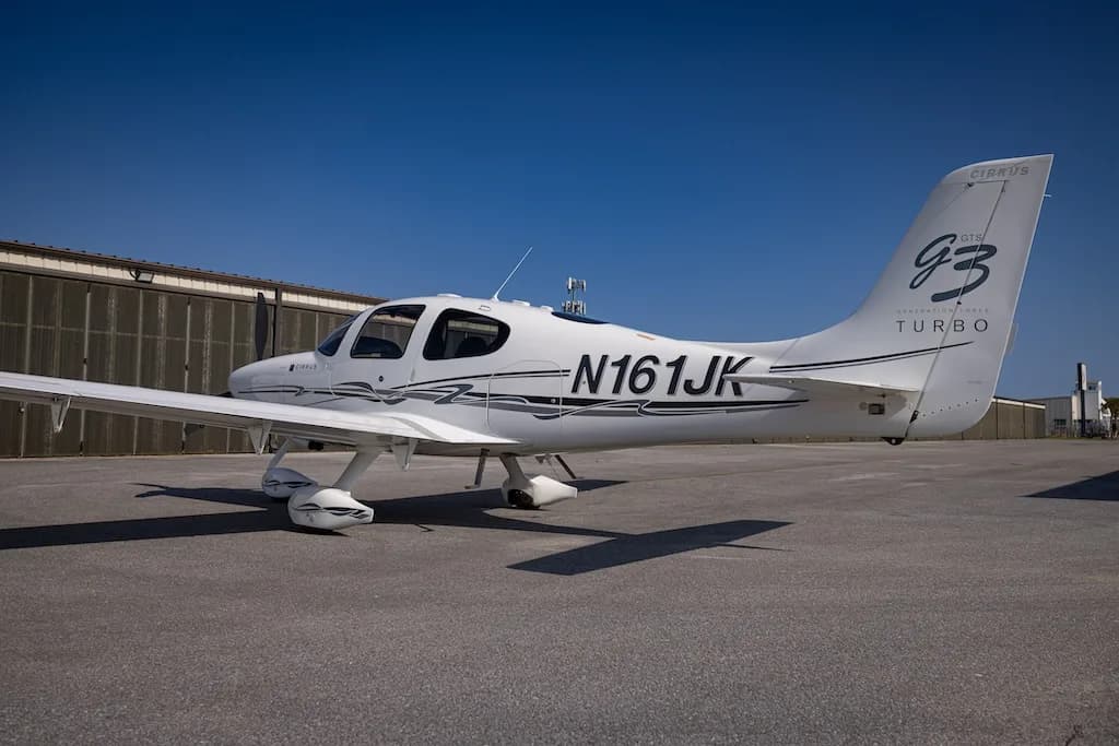 A white Cirrus SR22 G3 Turbo aircraft, registration N161JK, parked on an asphalt tarmac in front of hangars.