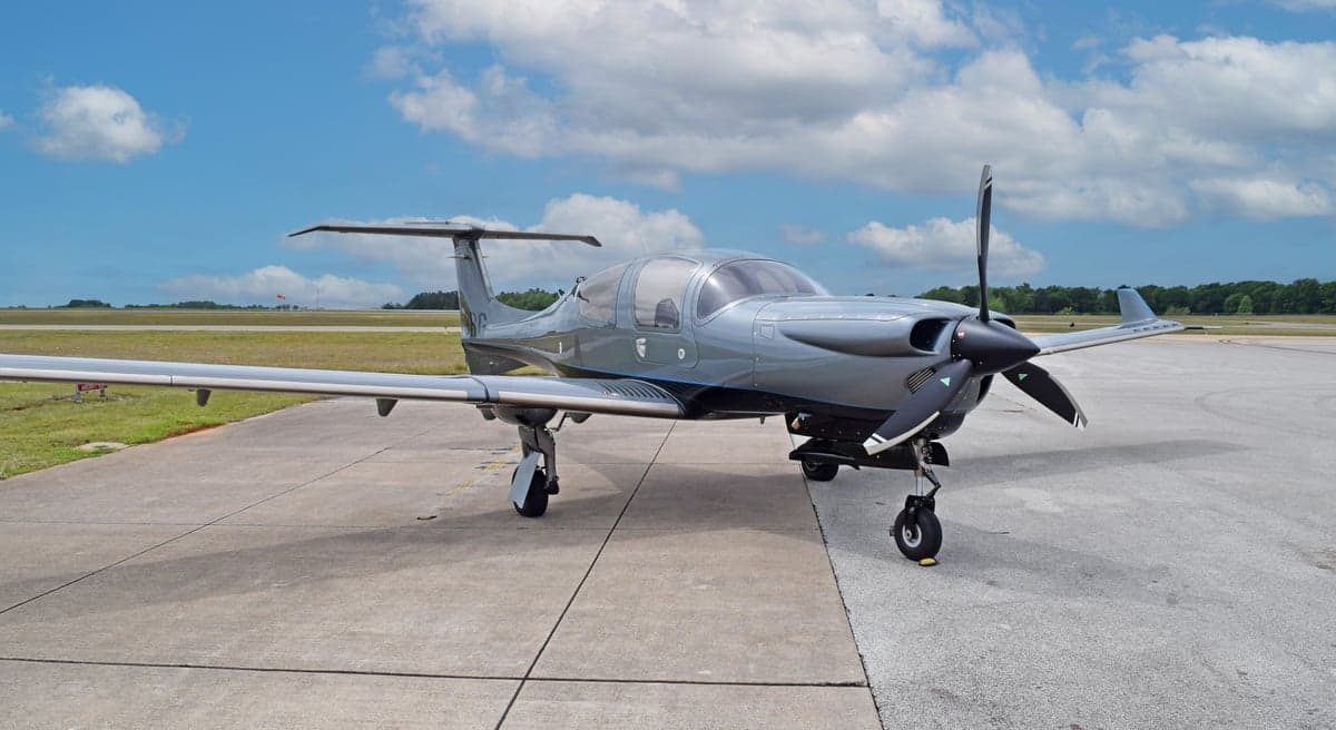 A gray Diamond DA50 RG aircraft, registration N59RG, with blue accents, parked on an airfield under a partly cloudy sky.