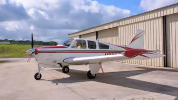 A Beechcraft Bonanza with a red and white paint scheme parked outside a hangar.