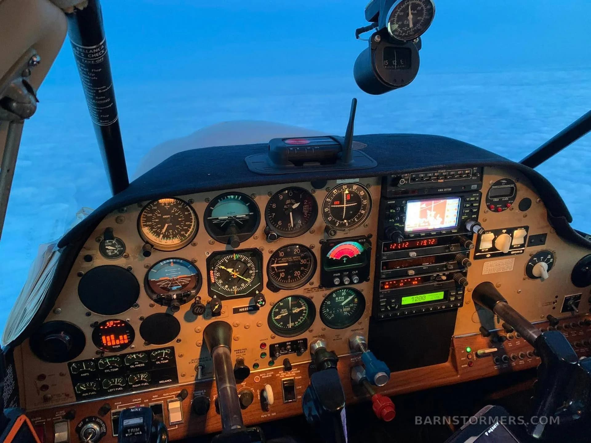 The instrument panel of a small aircraft, showing various gauges, avionics, and controls, with clouds visible outside the windshield.