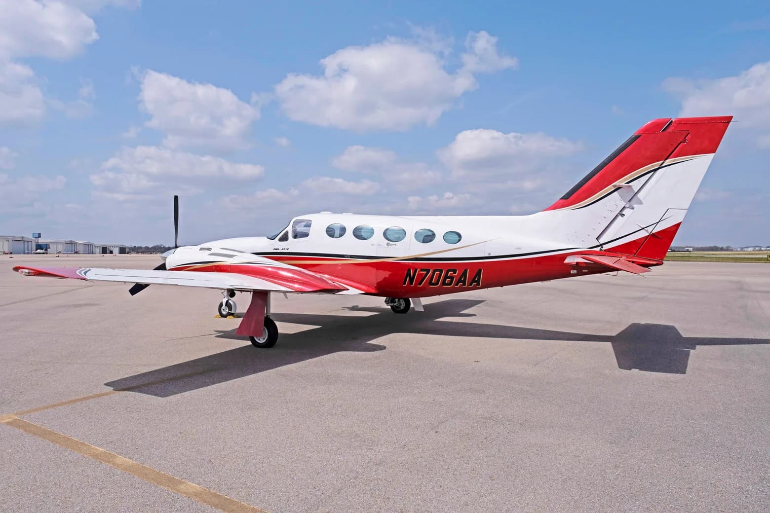 A side view of a white and red Cessna 421C Golden Eagle with registration N706AA on an airfield under a blue sky.