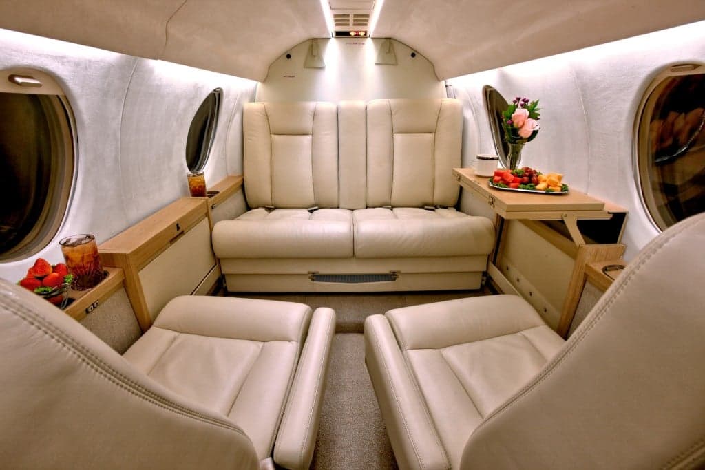 Interior view of the Hawker 4000 cabin with cream-colored leather seats and a small table with refreshments.