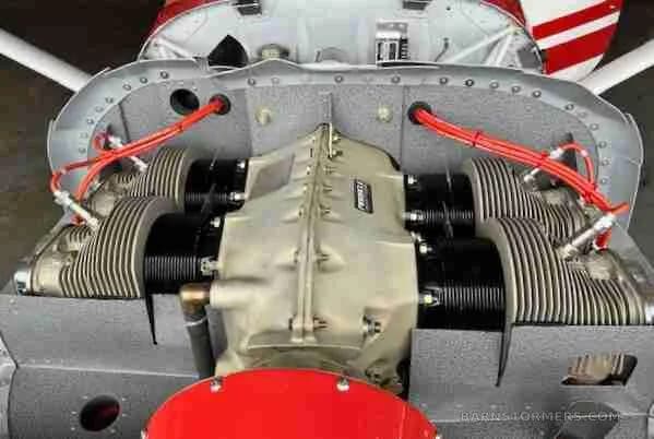 An overhead view of a four-cylinder aircraft engine with red ignition wires and exposed cooling fins.