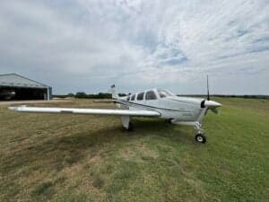 Beechcraft Bonanza N333SM parked on a grassy field near a hangar.