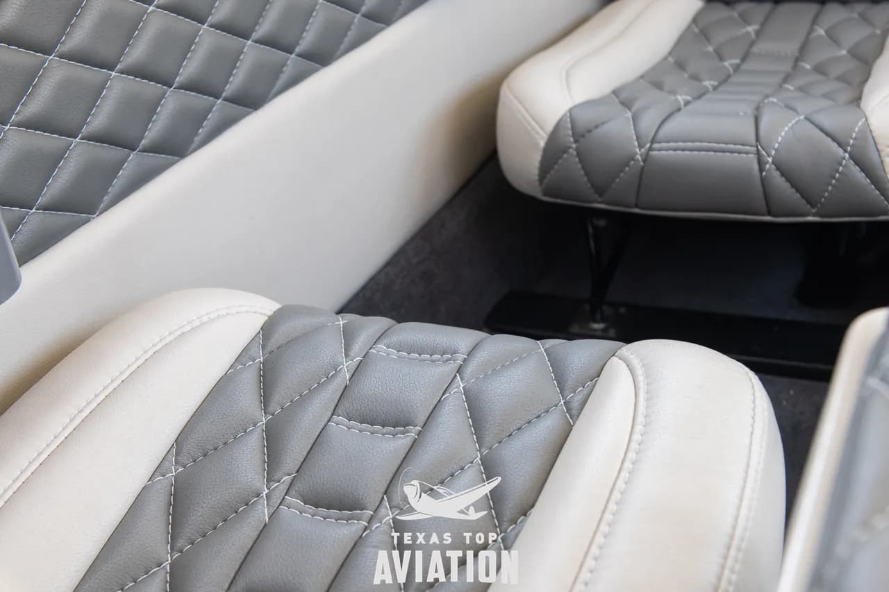 A close-up of the quilted white and grey seat upholstery and the carpeted floor in the aircraft cabin.