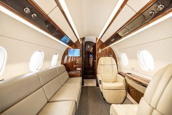 The luxurious interior cabin of the Embraer Legacy 500, featuring a beige couch and a single cream-colored seat.