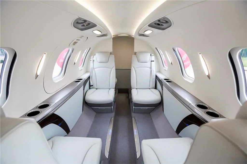 The bright, modern interior cabin of a HondaJet with white leather seats and large windows.