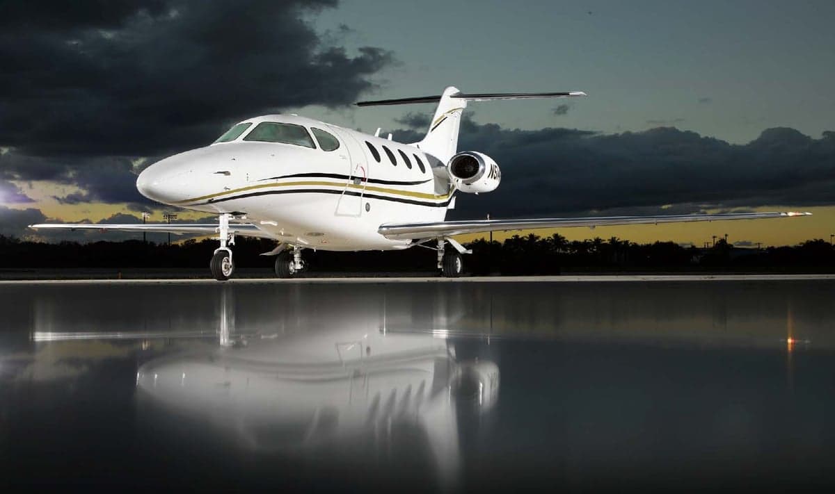 A Citation CJ3+ aircraft is parked on a reflective surface at sunset.
