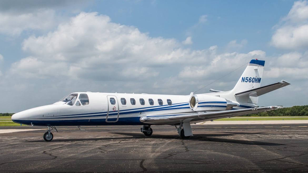 A Cessna Citation Encore sits on the tarmac with a blue and white paint scheme.