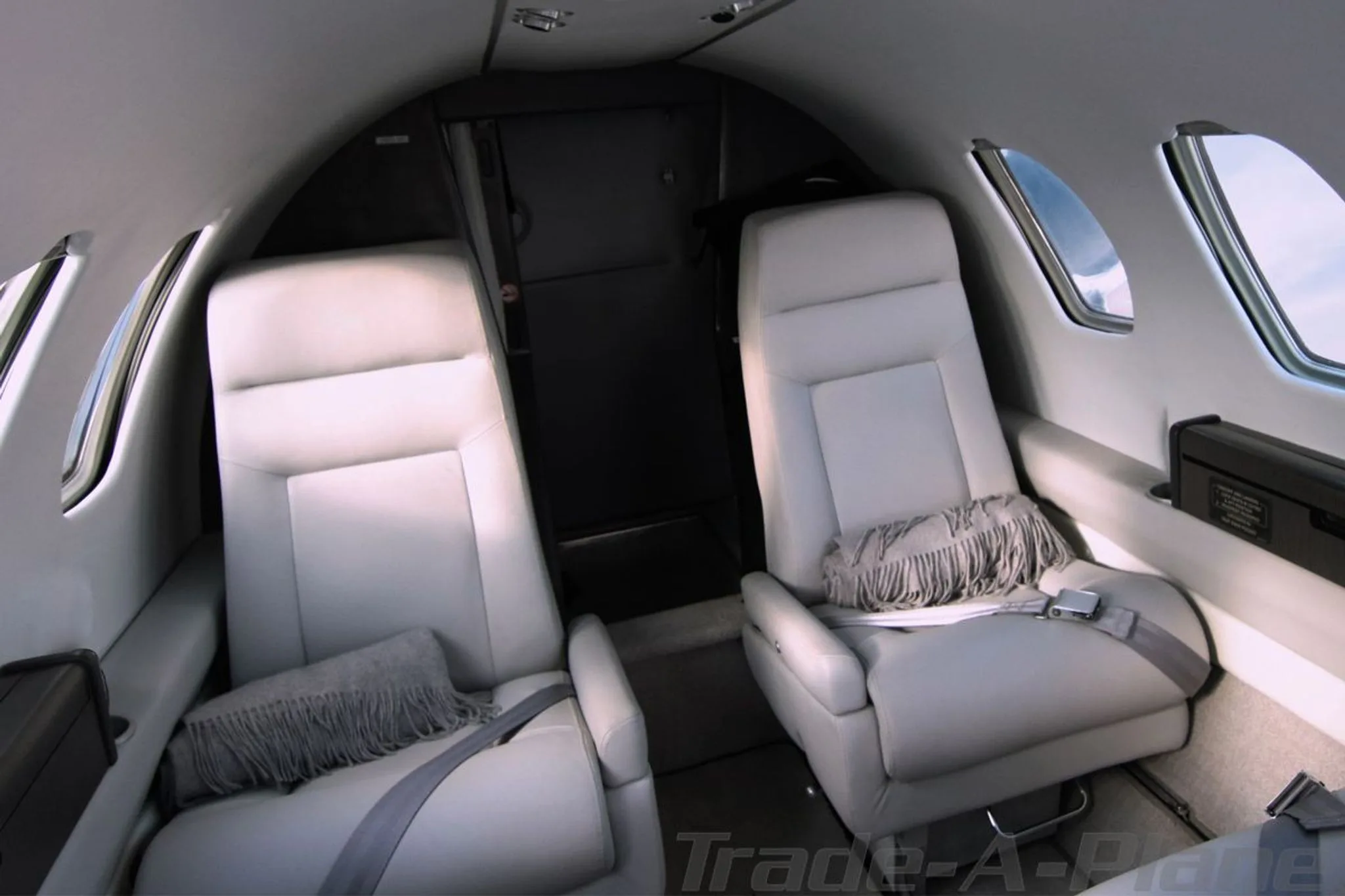 Two light gray leather cabin seats with gray throw blankets inside a Cessna CitationJet.