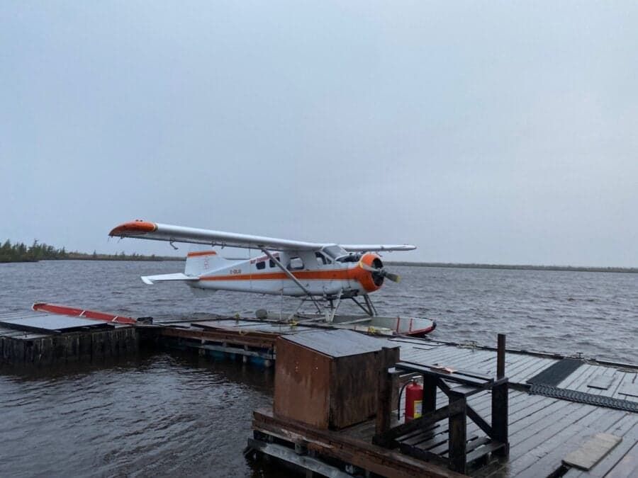 A de Havilland Beaver floatplane is docked on a wooden platform on a lake on a cloudy day.