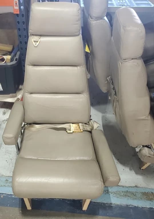 A single tan leather aircraft passenger seat with a seatbelt, likely removed from an aircraft.