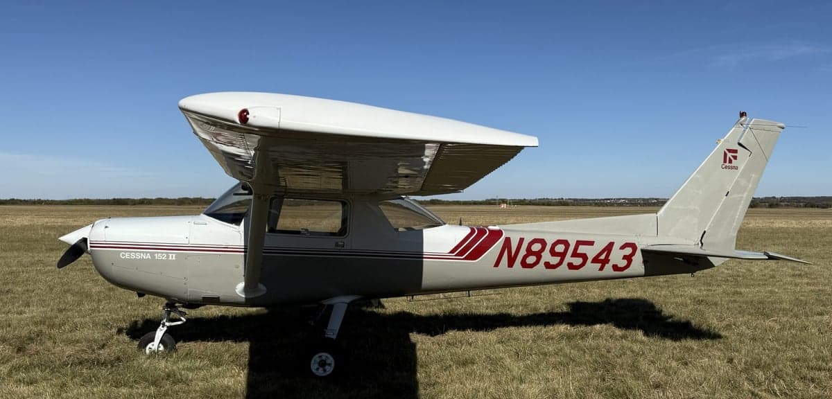 Side view of a Cessna 152 II aircraft with registration number N89543 parked on a grassy field.