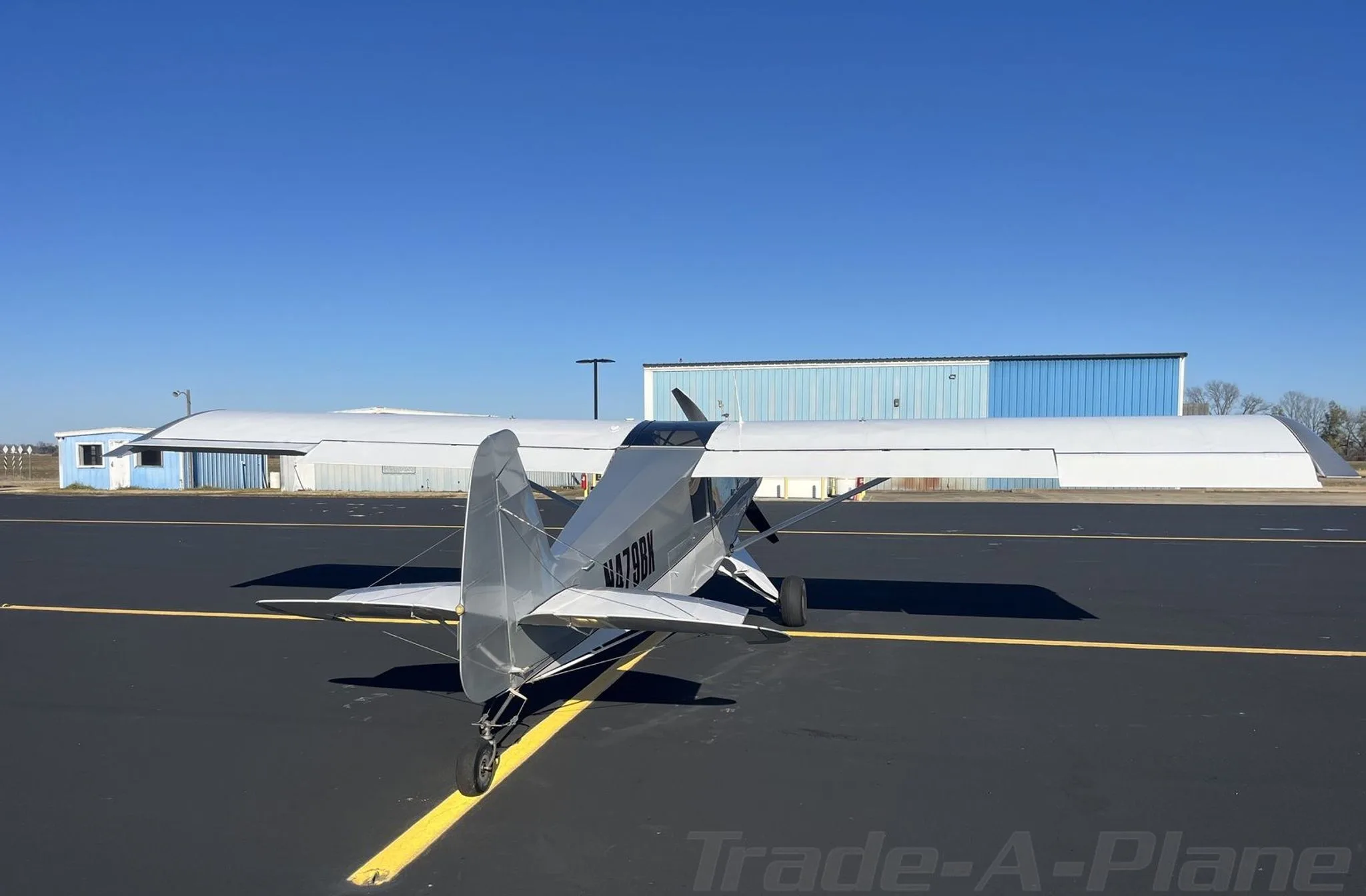 Rear view of a silver Bearhawk Patrol aircraft with registration N479BK on an asphalt tarmac with hangars in the background.