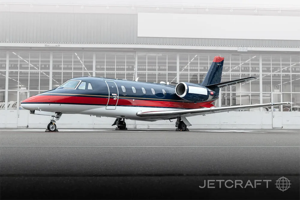 A dark blue, red, and white business jet parked on an asphalt apron, viewed from the side.