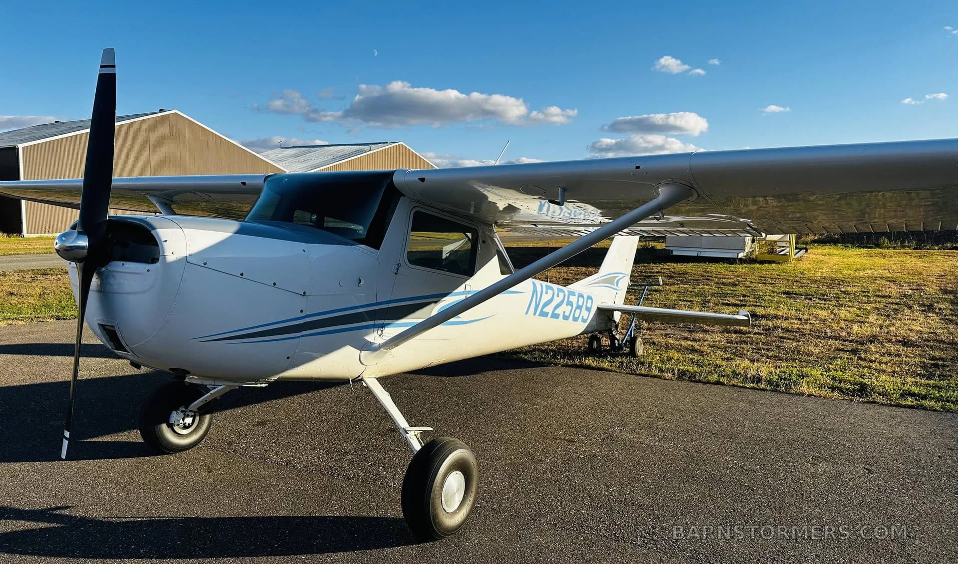 A three-quarter front view of a white Cessna 150/152 type aircraft with blue and grey stripes, tail number N22589, parked on an asphalt ramp.