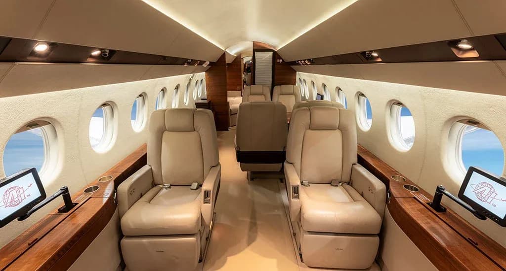The luxurious interior cabin of a business jet with light-colored leather seats and wood accents.
